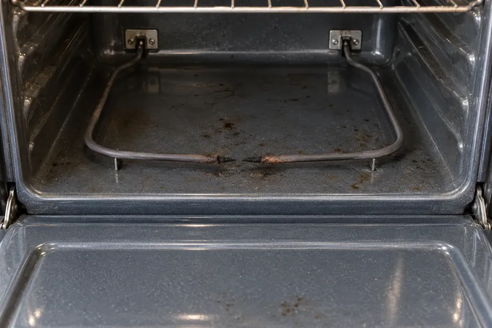 Inside of an electric oven with a fouled bake element and burnt residue on the oven floor