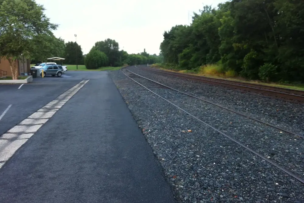 Railroad tracks running beside a paved lot and a line of trees in Pineville, North Carolina